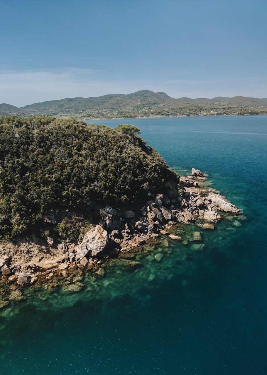 Vista aerea di un promontorio verde con scogliere dell'Isola d'Elba e acque trasparenti